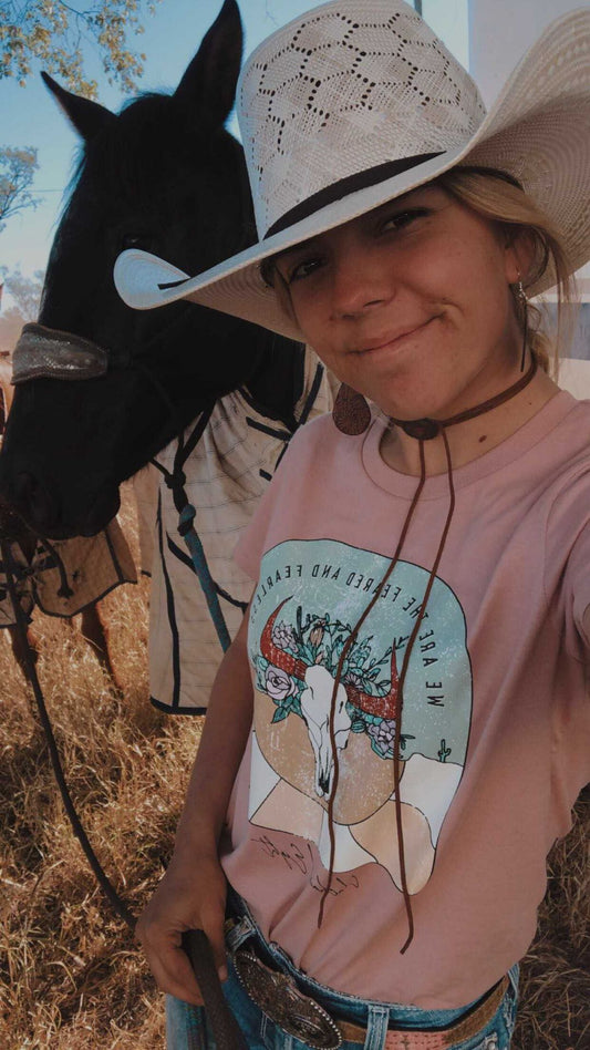 barrel racer in australia wearing feared and fearless unchained eight tee tshirt shirt with mavericks western straw hat next to stock horse. Australian cowgirl is wearing barrel racing buckle 