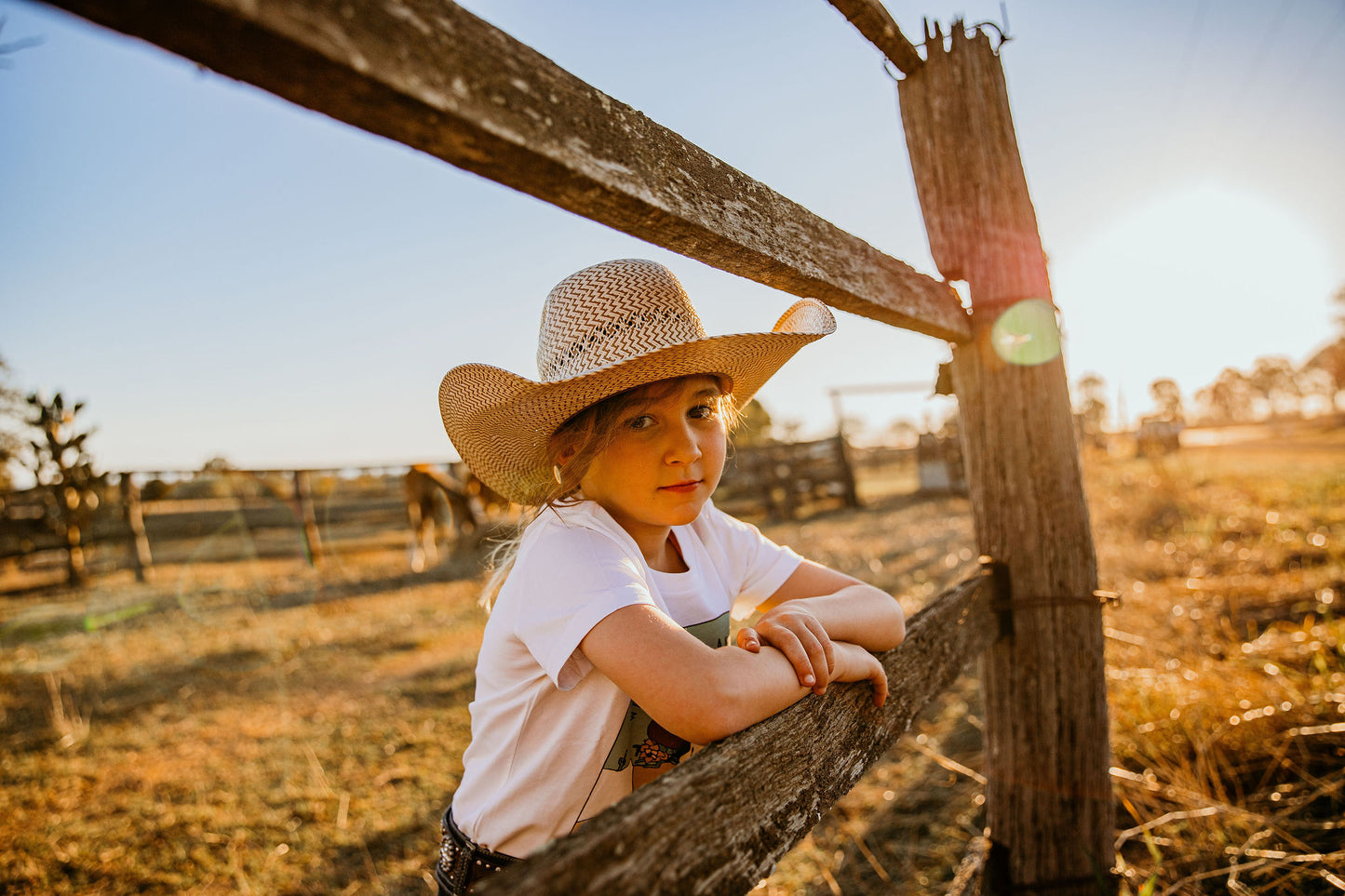 yong youth cowgirl kid wearing  we are the feared & fearless unchained eight country and western tee tshirt for kids youth and ladies shirt has flower cowskull with cactus and sunset. Wearing ariat belt in wrangler or mavericks western wear jeans top end bush boutique standing in paddock in rural australia ringers western cinch jeans little windmill clothing co mavericks western straw kids hat